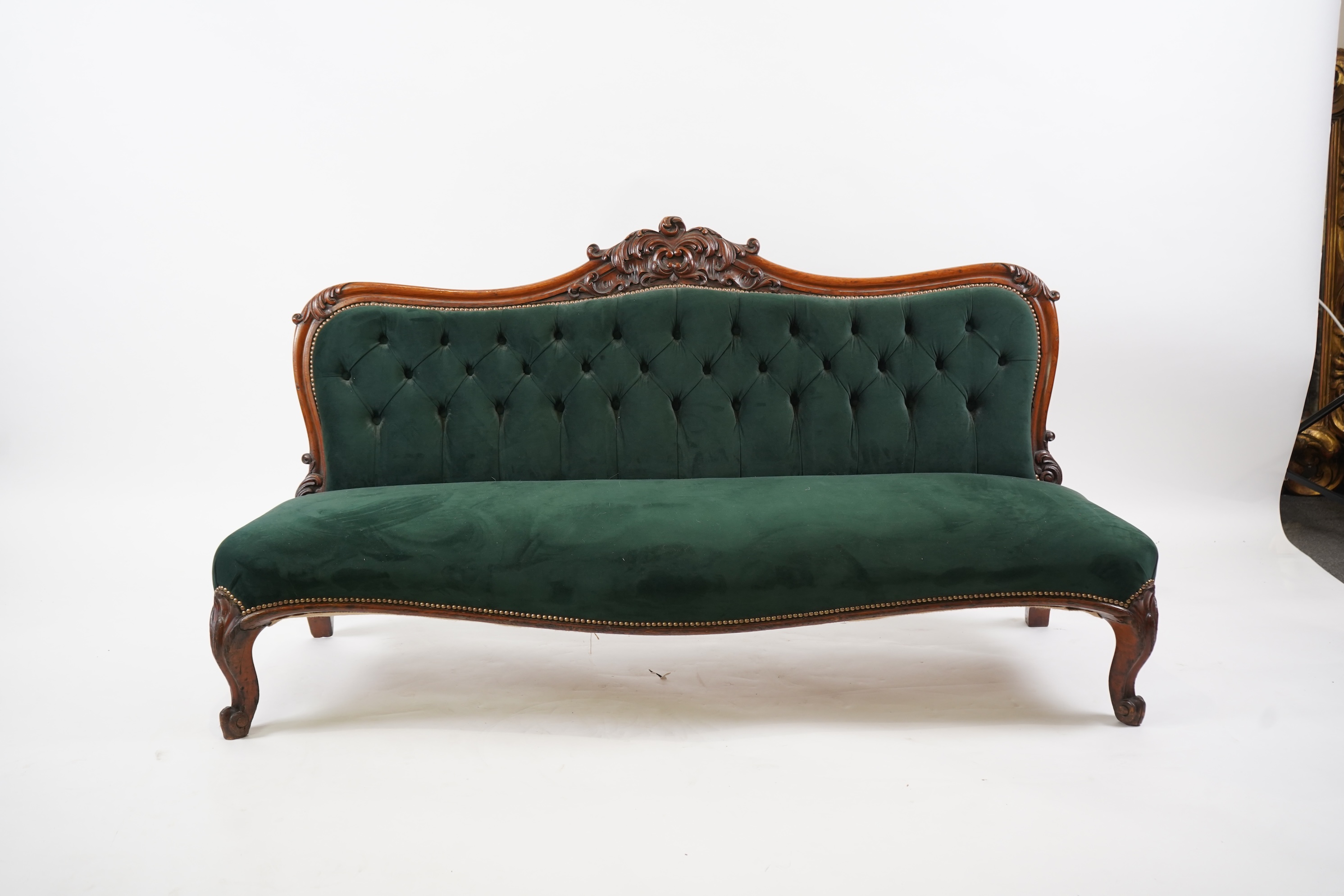 A pair of Victorian carved oak settees, recently re-upholstered in deep buttoned green velvet, the scroll carved crest rails over serpentine seats on cabriole front legs, 160cm wide, 96cm high, Provenance - previously gi